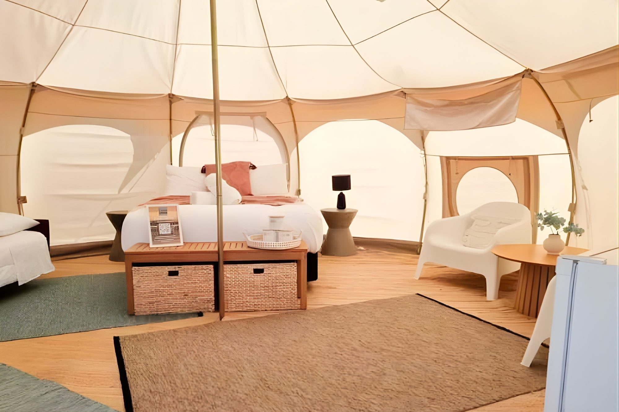 Spacious interior of a Better Bell glamping tent featuring a large bed, modern white lounge chair, and arched windows providing soft, natural light.