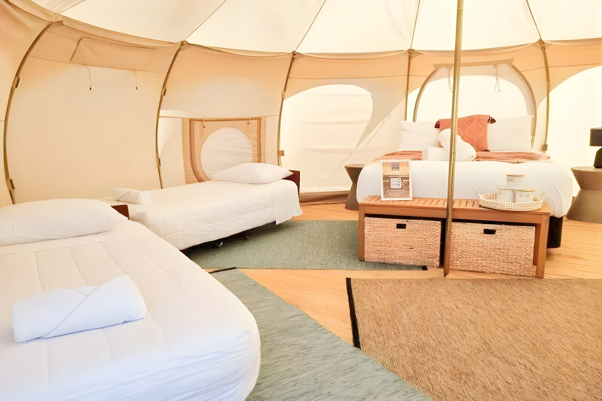 Spacious interior of an insulated Better Bell yurt tent configured with a large central bed and two single beds, showcasing a cozy, multi-person glamping layout.
